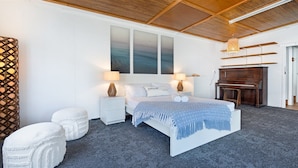 A bedroom with a bed, two nightstands, a piano, and a large window with artwork.