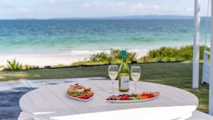 A table with a bottle of wine and two glasses, two plates of food, and a view of the beach.