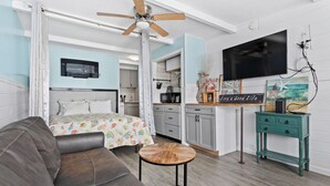 Ein Schlafzimmer mit Bett, Deckenventilator, Fernseher und einer Küchenzeile.