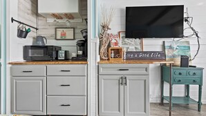 Eine Küche mit Mikrowelle, Kaffeemaschine und einem flachbildfernseher an der Wand.