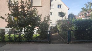 A residential building with a gated entrance, a small pathway leading to the entrance, and a tree with green leaves in the foreground.