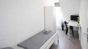 A small, modern room with a single bed, a desk, and a chair.