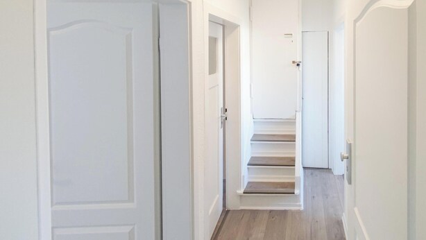 A narrow hallway with white doors and wooden flooring leading to a staircase.