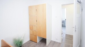 A room with a wooden wardrobe, a bed, a potted plant, and a doorway leading to another room.