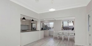 Una cocina moderna con armarios blancos, un comedor con sillas blancas y vistas al exterior a través de una ventana.