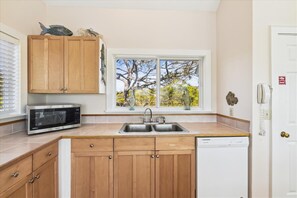A kitchen with wooden cabinets, a microwave, a dishwasher, and a window with a view of trees.