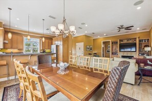 A spacious living area with a wooden dining table, comfortable seating, a television, and a bookshelf.