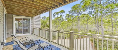 A covered deck with outdoor furniture and a view of a forest.