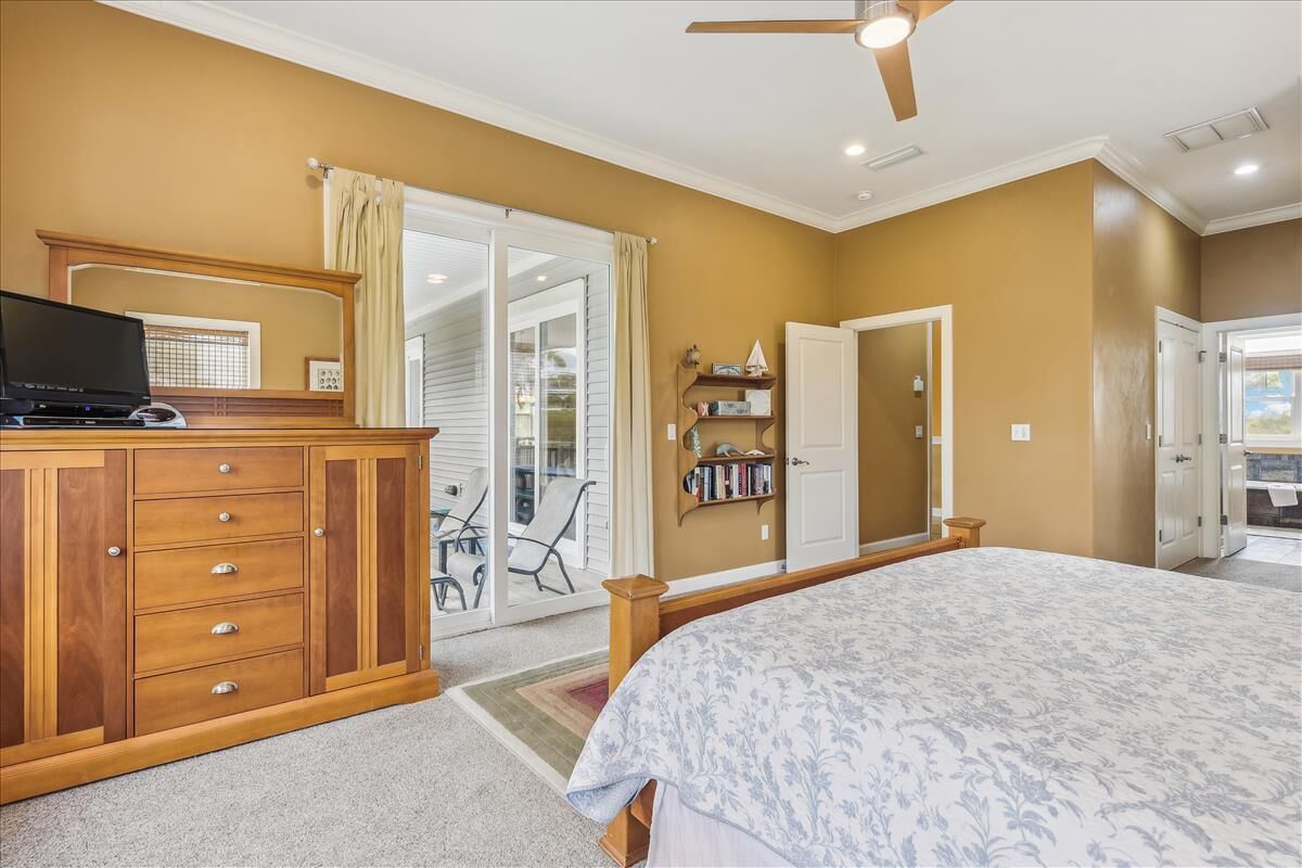 A bedroom with a bed, a wooden dresser, a ceiling fan, and a sliding glass door leading to a balcony.