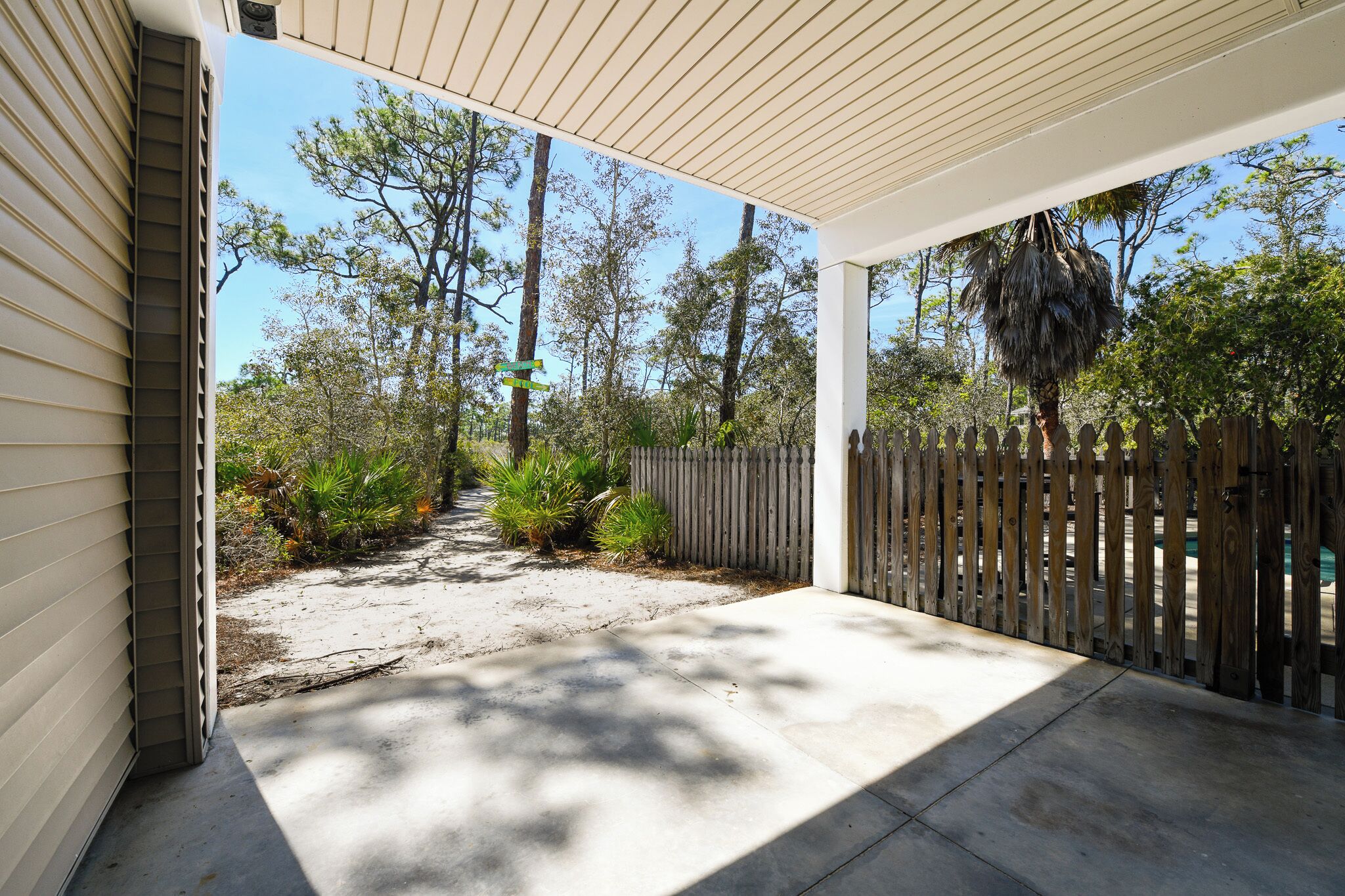 A covered patio with a concrete floor, a wooden fence, and trees in the background.