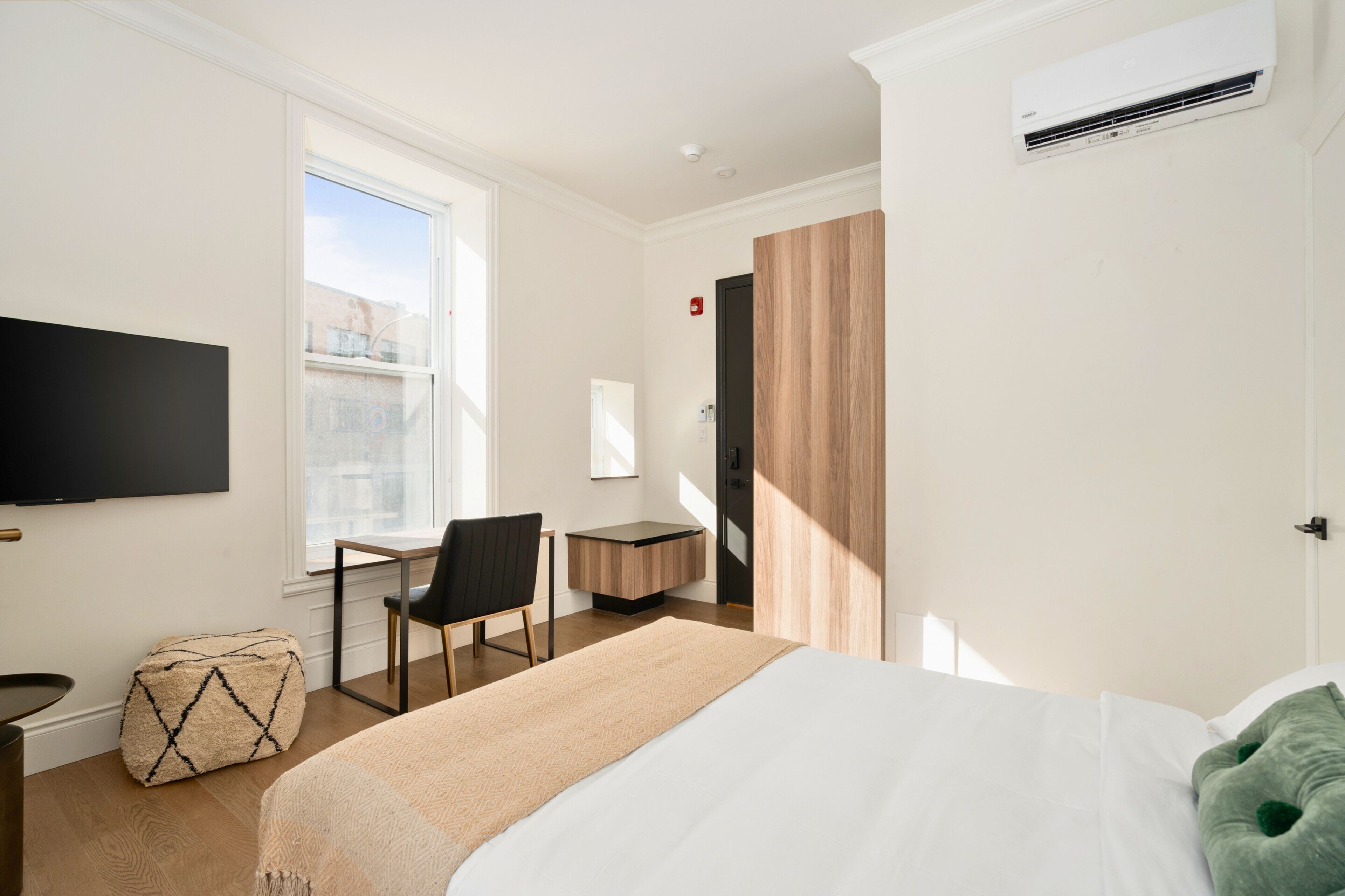 A modern hotel room with a bed, a desk, a chair, a television, and a window.