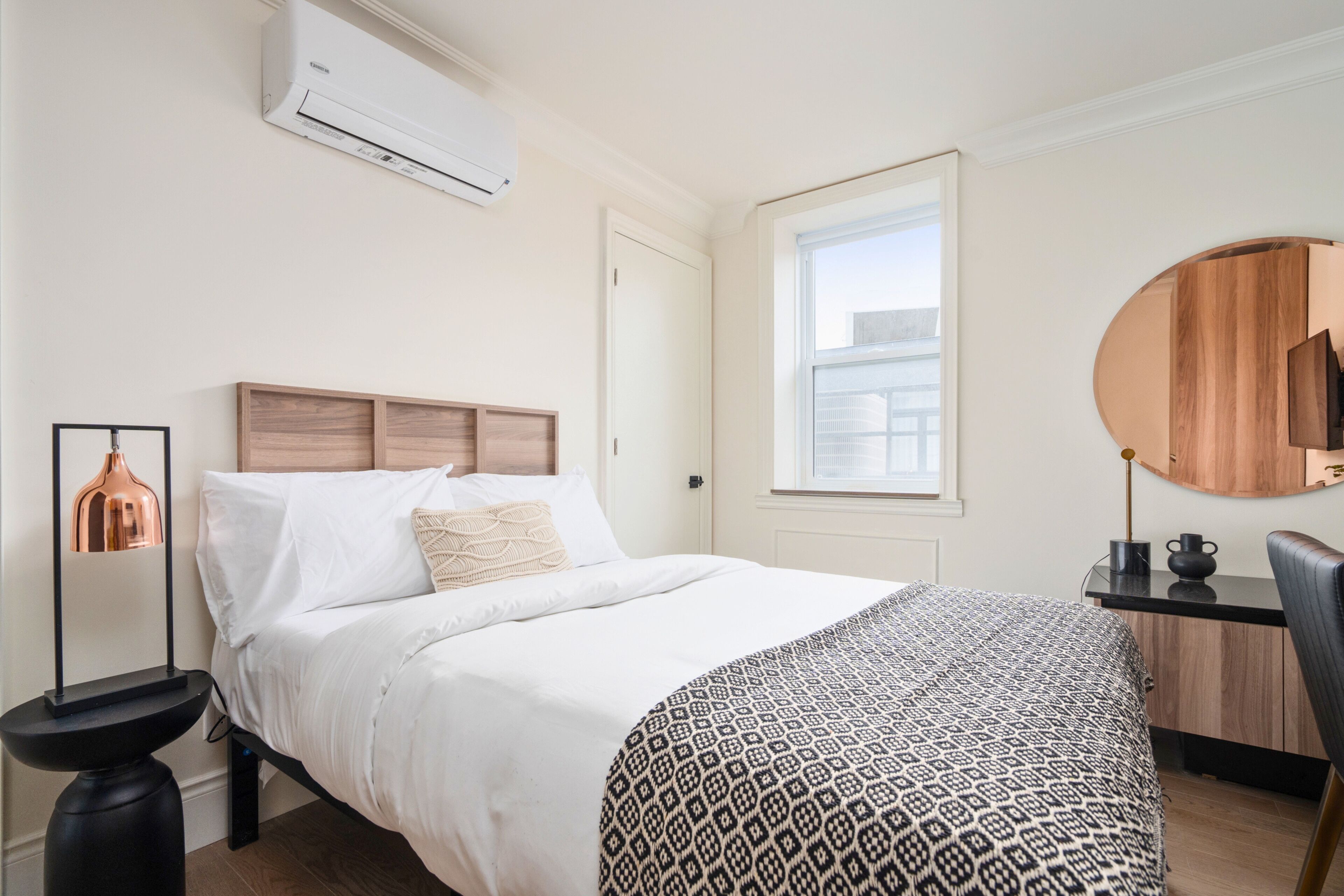 Une chambre à coucher avec un lit, une table de chevet, un miroir et une fenêtre.