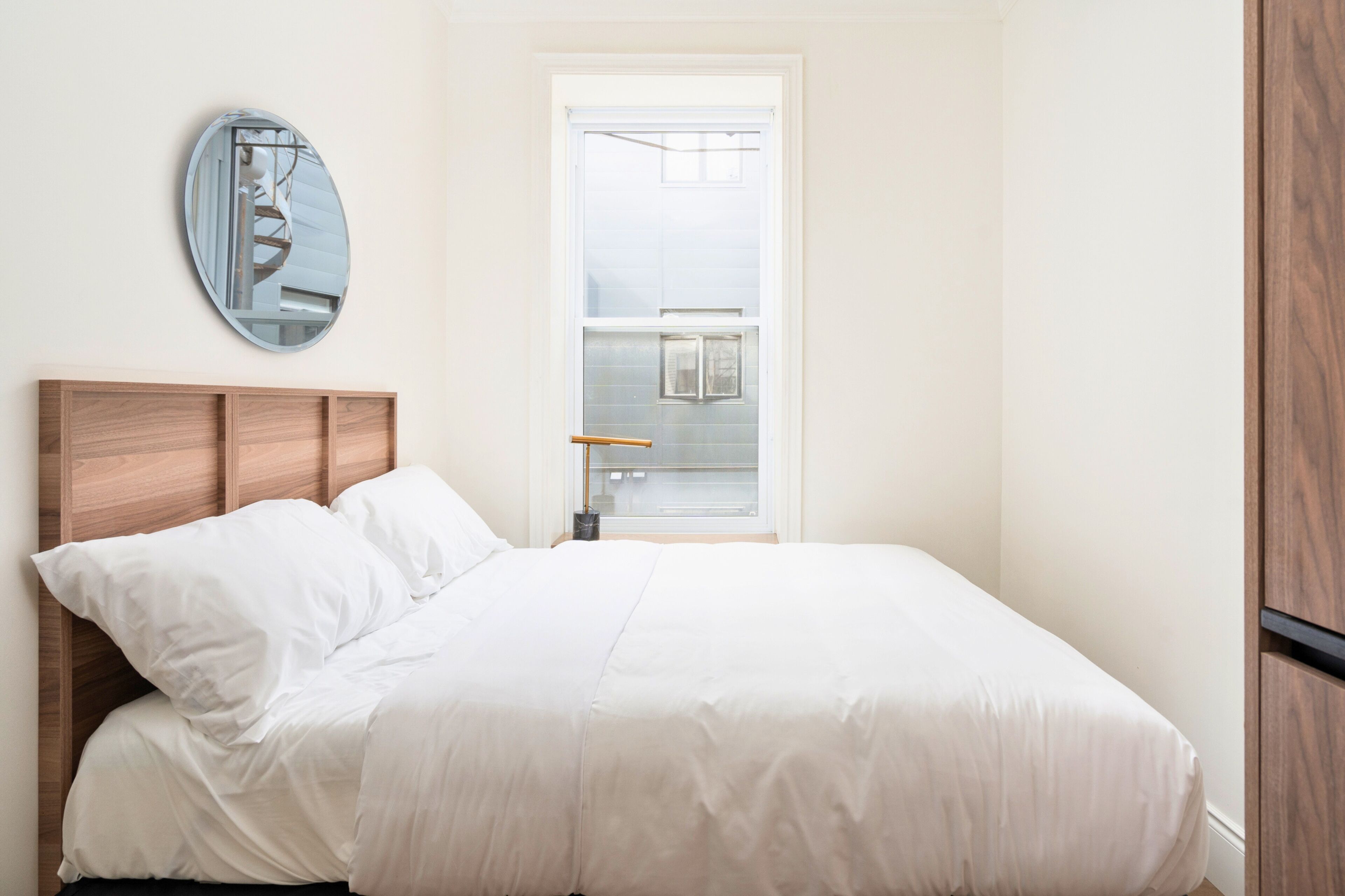 Un dormitorio con cabecera de madera, un espejo grande y una ventana con vista a un edificio.