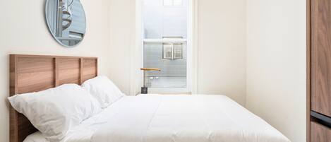Un dormitorio con cabecera de madera, un espejo grande y una ventana con vista a un edificio.