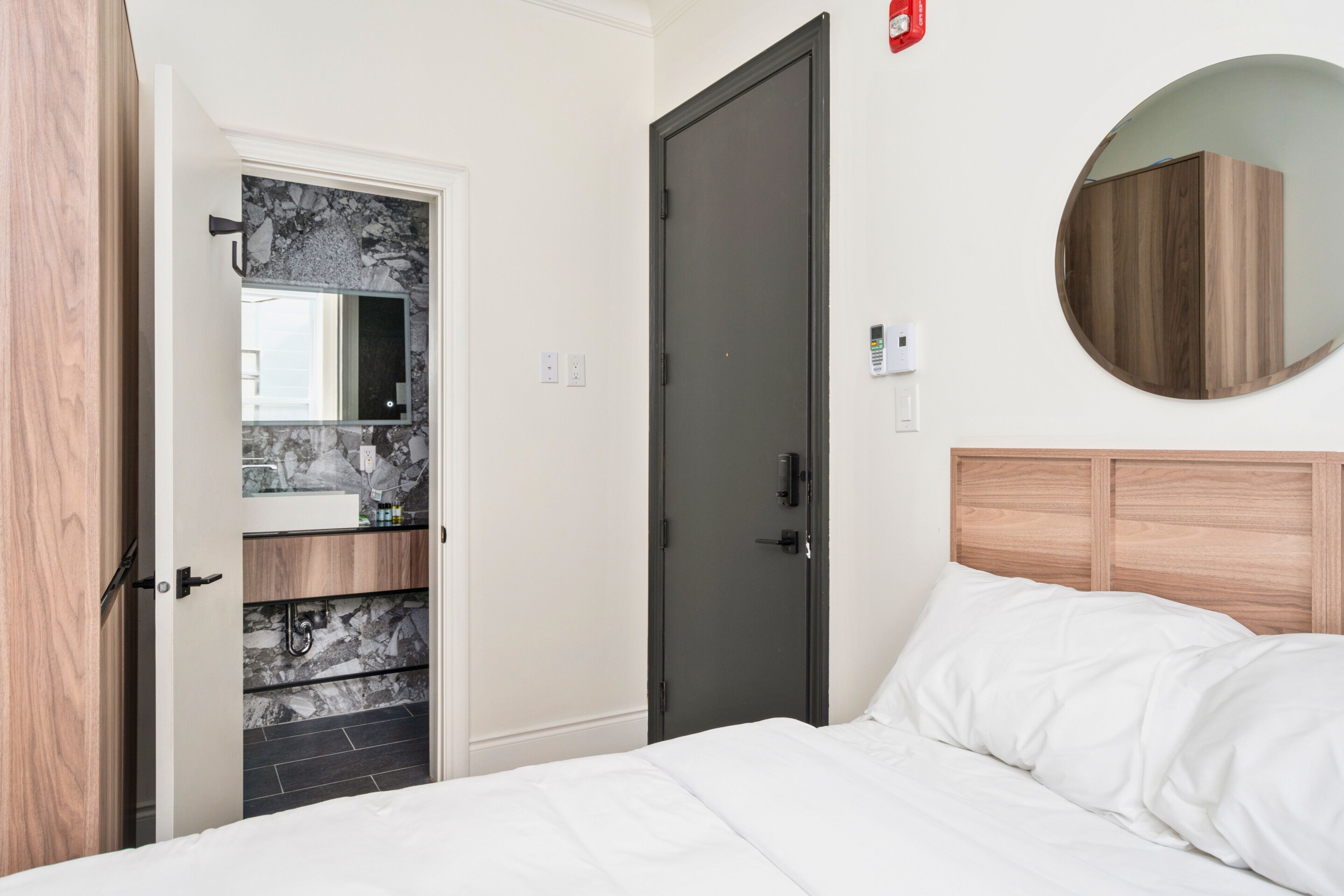 Een hotelkamer met een bed, een kledingkast, een badkamer met een marmeren wastafel en een ronde spiegel aan de muur.