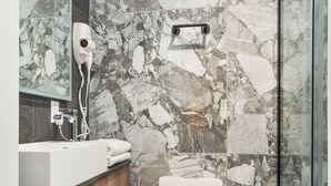 A modern bathroom with a marble wall, a white sink, and a glass shower enclosure. - Opal Lofts - Quartier Latin (Montreal)