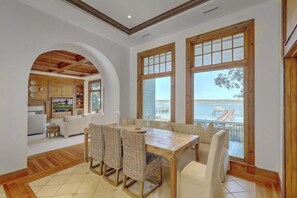 Un'area pranzo con tavolo in legno e sedie in vimini, una cucina con mobili in legno e ampie finestre vista mare.