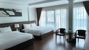 A hotel room with two beds, a ceiling fan, a desk with a chair, and large windows with sheer curtains. - THE WILTONS HOTEL LAO CAI (Lao Cai)