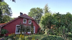A red house with a sloped roof, surrounded by lush greenery and trees. - Idyllic fisherman's house, modern and friendly, close to the beach (Varel)
