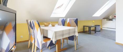 A dining area with a table and chairs, a small kitchen area, and a ceiling with skylights.