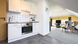 A modern kitchen with white cabinets, a built-in oven, and a microwave. There is a dining area with a table and chairs. - Idyllic fisherman's house, modern and friendly, close to the beach (Varel)