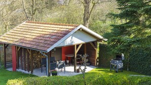 A rustic wooden structure with a tiled roof, a covered patio with seating, and a barbecue grill. - Idyllic fisherman's house, modern and friendly, close to the beach (Varel)