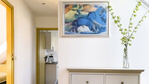 A hallway with a white wall, a painting of blue horses, a white cabinet with drawers, and a door leading to another room. - Idyllic fisherman's house, modern and friendly, close to the beach (Varel)