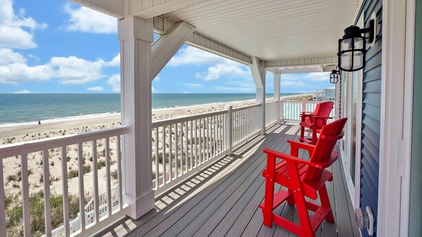 A covered porch with a view of the beach, featuring a railing and red chairs. - BonBini: Oceanfront 7-bedroom house in Oak Island, perfect for large groups. (Oak Island)