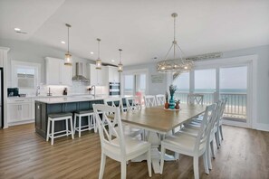 A modern kitchen with white cabinetry, a wooden dining table, and a view of the ocean.