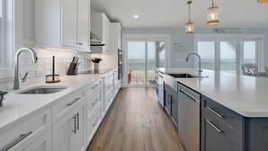 A modern kitchen with white cabinetry, stainless steel appliances, and a large island. - BonBini: Oceanfront 7-bedroom house in Oak Island, perfect for large groups. (Oak Island)