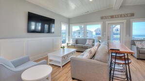 Un vaste salon doté d’un grand téléviseur à écran plat, d’une table basse en bois et d’un ensemble de canapés. Un panneau indiquant « Oak Island » est visible sur le mur.