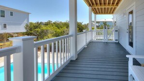 Une terrasse en bois couverte, dotée de rampes blanches, une piscine et une vue dégagée sur les environs.