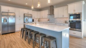 Une cuisine moderne avec des meubles blancs, des appareils en acier inoxydable et un îlot central doté de tabourets de bar.