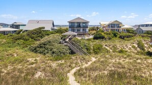 A coastal property with a prominent house featuring a large balcony, a covered patio, and a staircase leading to the entrance. - Discover Peace on the Beach, a stunning 6BR, 5BA oceanfront retreat in Oak Island. (Oak Island)