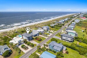 An aerial view of a coastal residential area with houses, a beach, and a lighthouse.