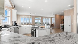 A spacious kitchen with a granite countertop, white cabinetry, and a central island. - Discover Peace on the Beach, a stunning 6BR, 5BA oceanfront retreat in Oak Island. (Oak Island)