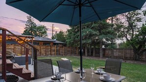 En udendørs terrasse med et spisebord, omgivet af stole og en parasol.