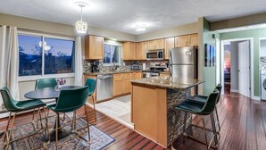 A modern kitchen with wooden cabinets, stainless steel appliances, and a dining area with green chairs. - Cozy Denver Stay | Grill + Patio | Sloan’s Lake| Firepit (Denver)