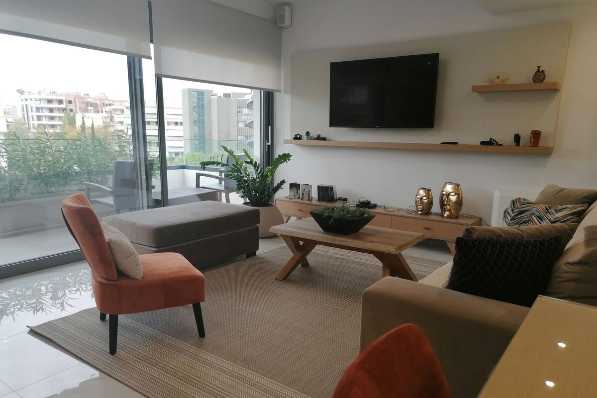 A modern living room with a sofa, armchair, coffee table, and a TV mounted on the wall.