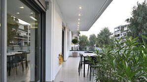 Un espacio moderno para comer al aire libre con pared de vidrio, una mesa, sillas y plantas en macetas.