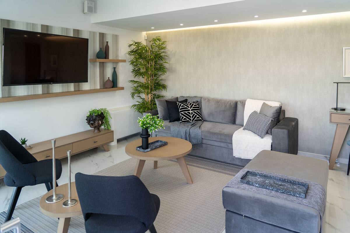 A modern living room with a flat-screen TV, a grey sofa, a coffee table, and a side table with a plant.