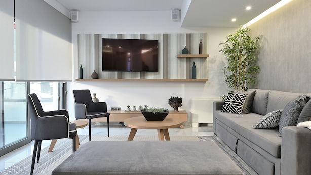 Una sala de estar moderna con un sofá gris, sillas blanco y negro, una mesa de centro redonda y un televisor grande montado en la pared.