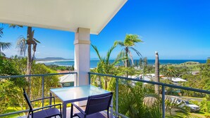 A balcony with a glass table and chairs, overlooking a coastal landscape with palm trees and a view of the ocean. - Breakers 2 2/13 East Street (Crescent Head)