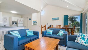 A living room with two sofas, a wooden coffee table, a dining area with a table and chairs, and a kitchen in the background.