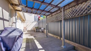 A covered outdoor area with a patio table and chairs, a grill, and a wooden fence.