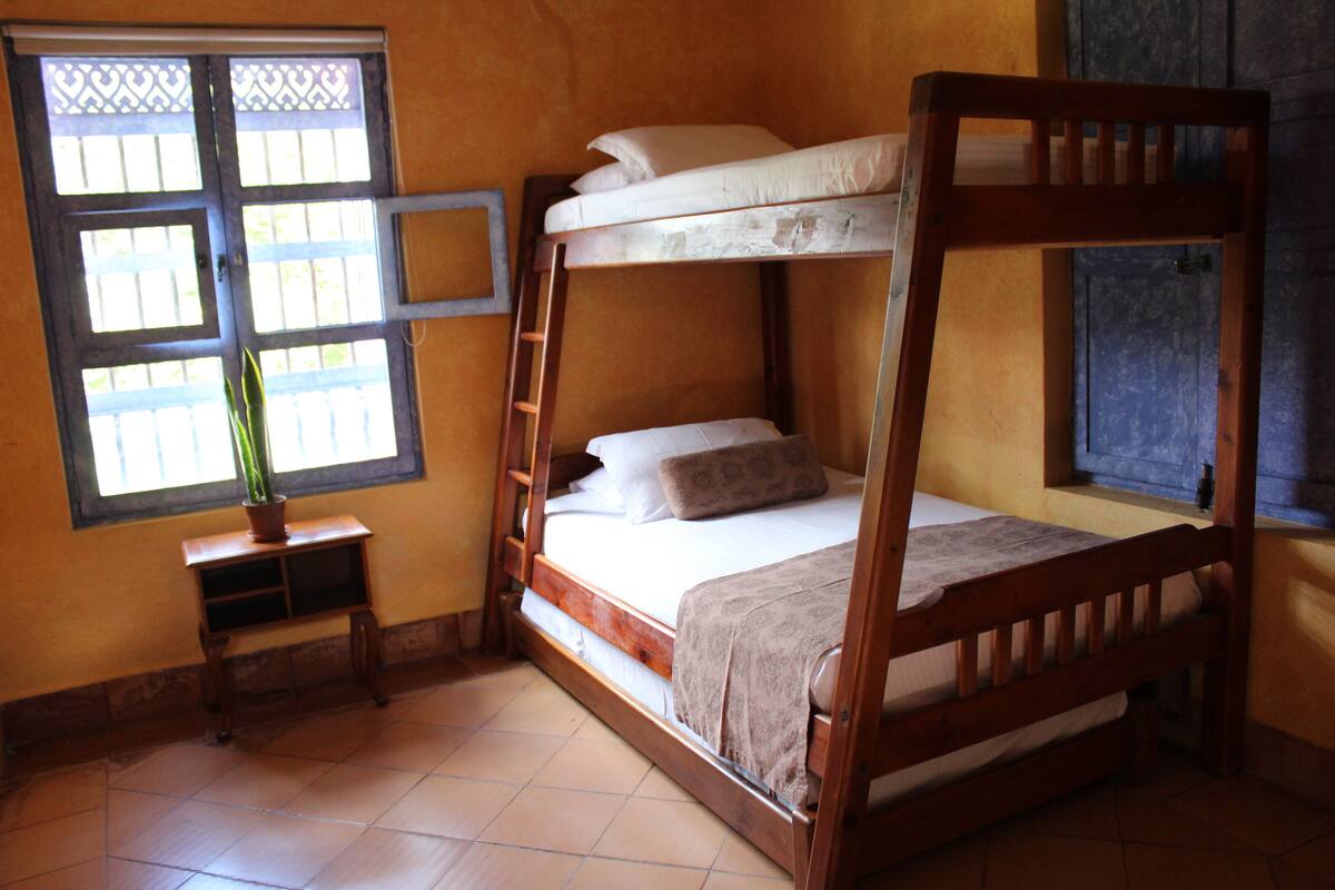 A wooden bunk bed with a ladder, a small bedside table, and a potted plant.