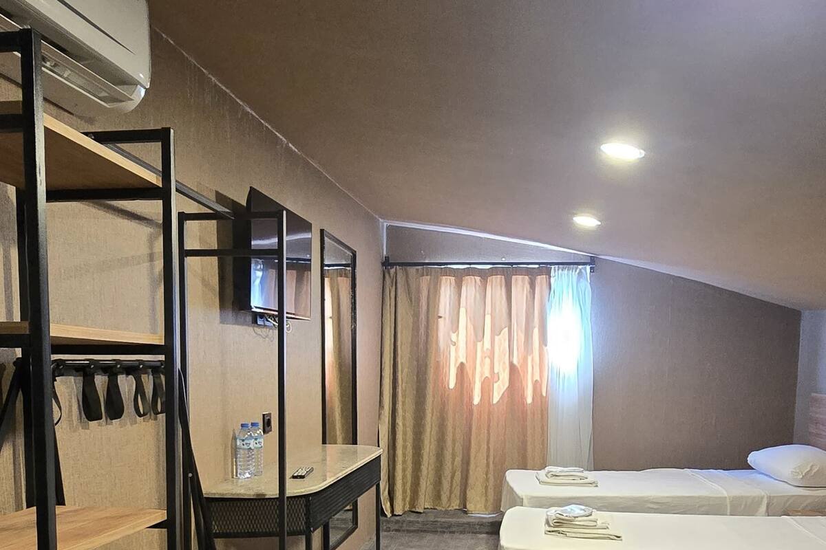 Habitación de hotel con literas, un escritorio, una silla, un televisor y una ventana con cortinas.