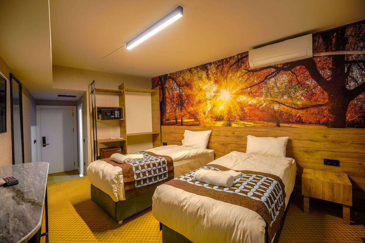 Habitación de hotel con dos camas, un escritorio, una silla, microondas y un mural grande con motivos otoñales.