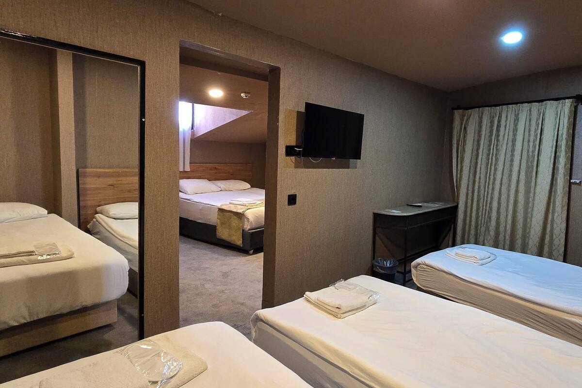 Habitación de hotel con dos camas, un televisor montado en la pared y una mesita.