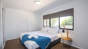 A neatly arranged bedroom with a bed, a bedside lamp, and a window with a view of greenery. - 25 A Twynam Street, Jindabyne (Jindabyne)